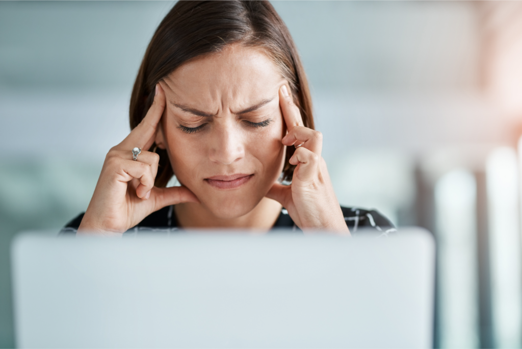 Woman in front of a computer grasping her head due to a headache.