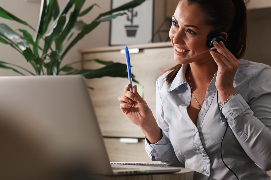 Woman holding a pen speaking into a headset at work.